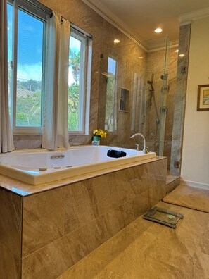 Ein modernes Badezimmer mit einer großen Badewanne, einer Duschkabine und Blick auf Grünflächen.