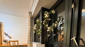 A room with a wooden desk, a chair, a potted plant, and a window with a curtain. - Cosy Apartment in Canary Wharf  (London)