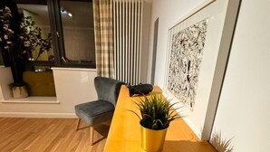 A modern living room with a wooden coffee table, a grey sofa, a potted plant, and a framed abstract painting on the wall. - Cosy Apartment in Canary Wharf  (London)