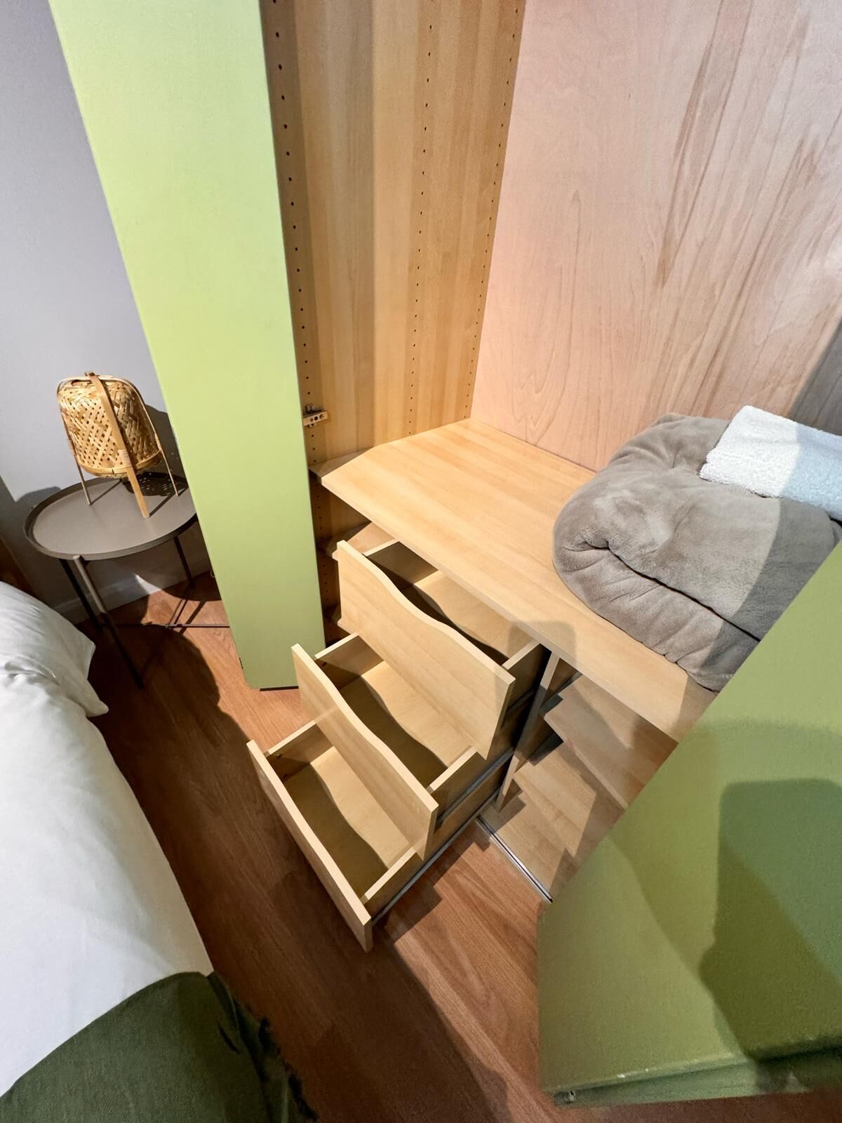 A compact room with a bed, a small round table, a wicker chair, and a built-in bench with a cushion.