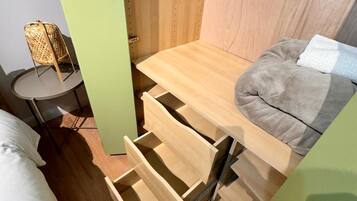 A compact room with a bed, a small round table, a wicker chair, and a built-in bench with a cushion.