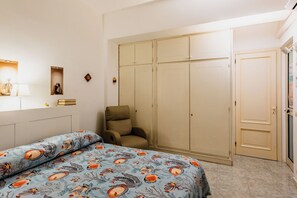 A bedroom with a bed, a chair, a wardrobe, and a bedside table with a lamp. - Coralie House (Giardini Naxos)