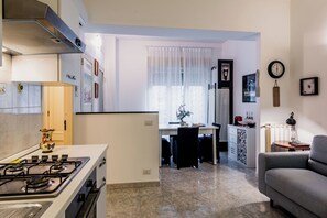 A modern kitchen with a gas stove, a dining area with a table and chairs, and a living room with a sofa. - Coralie House (Giardini Naxos)