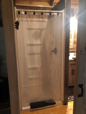 Une salle de bain avec un rideau de douche, une porte en bois et une petite marche menant à l’espace de la douche.