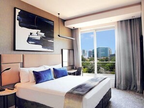Relax in a spacious room with a large bed, city skyline views, and a beautiful abstract art piece above.