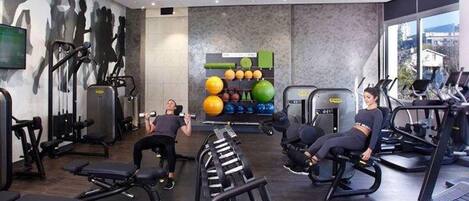 Un gimnasio con equipo de ejercicio variado, incluyendo cintas de correr, máquinas de pesas y una pared con pelotas de ejercicio.