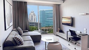 Ein modernes Hotelzimmer mit großem Fenster, einer Sitzecke, einem runden Couchtisch, einem Fernseher und einem Schreibtisch mit Stuhl.