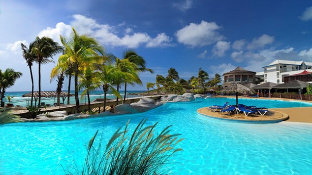 A resort pool with palm trees, lounge chairs, and a view of the ocean. - Sea view studio with water tank (Saint-François)