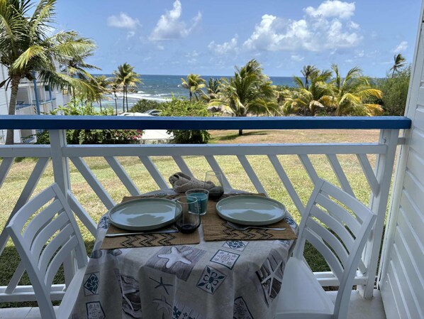 A table set for two with plates, glasses, and a fork on a deck with a view of the ocean and palm trees.