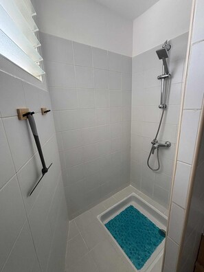 A small, tiled shower area with a blue bath mat, a handheld showerhead, and a handheld shower attachment.