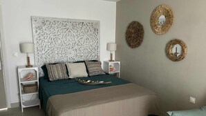 A bedroom with a patterned headboard, two bedside tables with lamps, a bed with a teal and beige bedspread, and three wall decorations. - Sea view studio with water tank (Saint-François)