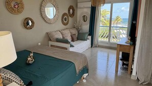 A bedroom with a bed, a desk, and a view of the ocean. - Sea view studio with water tank (Saint-François)