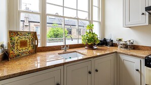 A kitchen with a large window, a sink, cabinets, and a countertop with various items. - Classic Luxury in Central London (London)