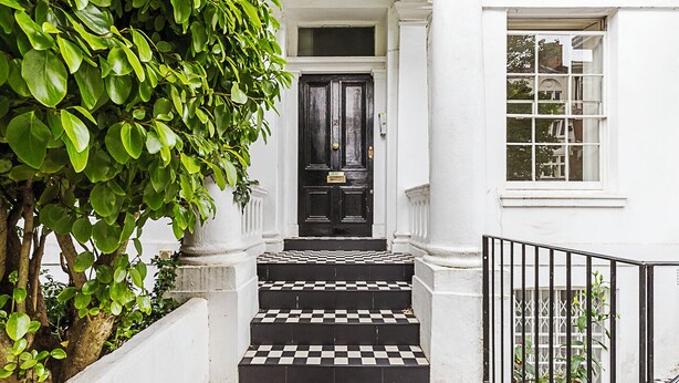 A black and white checkered staircase leading to a black door with a brass knocker, flanked by white columns and a white wall. - Classic Luxury in Central London (London)