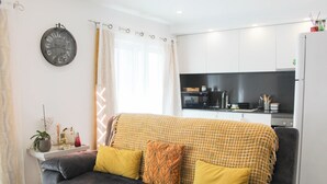 A modern living room with a grey sofa, yellow cushions, and a kitchen in the background. - Blossom Cozy Home (Ponta Delgada)