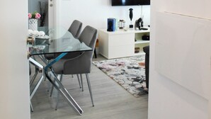 A modern living room with a glass dining table, grey chairs, a flat-screen TV, and a white sofa. - Blossom Cozy Home (Ponta Delgada)