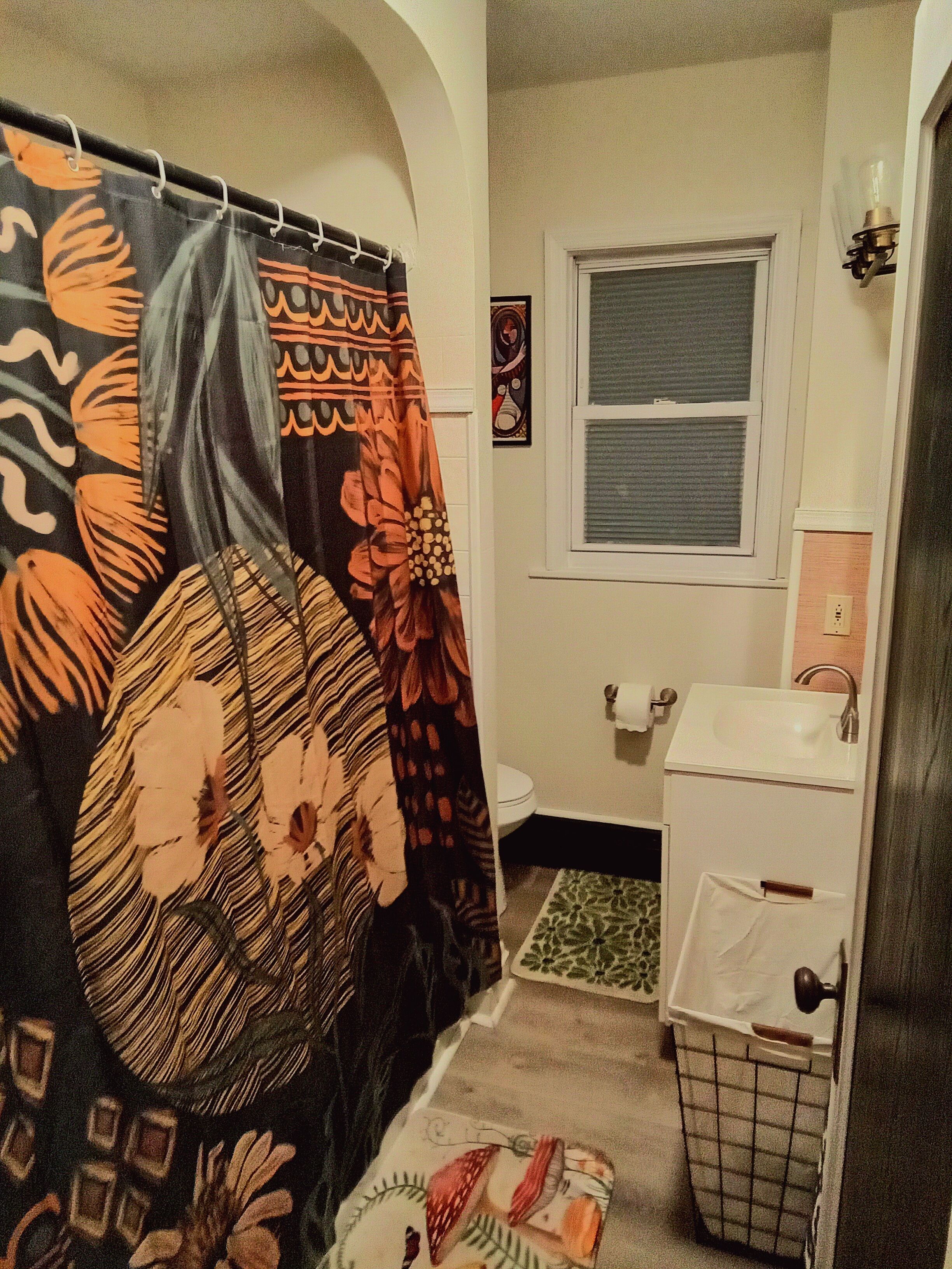A bathroom with a shower curtain, toilet, sink, and a window.