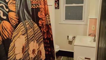 A bathroom with a shower curtain, toilet, sink, and a window.
