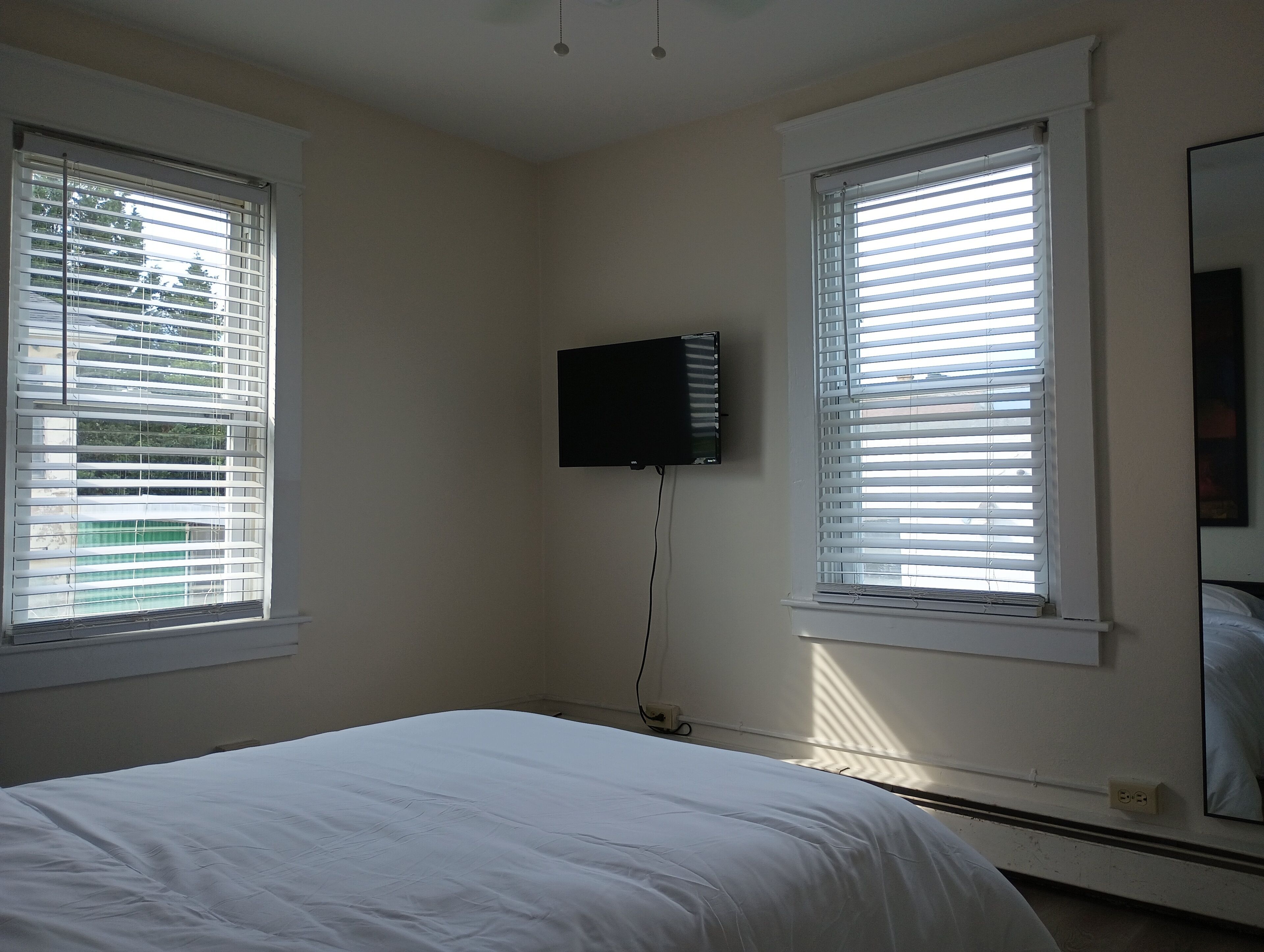 Un dormitorio con dos ventanas, una cama y un televisor montado.