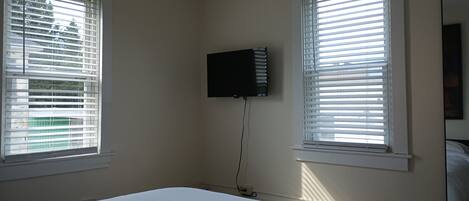 Un dormitorio con dos ventanas, una cama y un televisor montado.