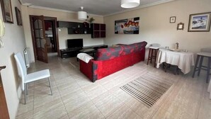 A living room with a red sofa, a white chair, a TV, and a kitchen area with cabinets and a white ceiling light. - Mikasita: spacious house with mountain views (PV)