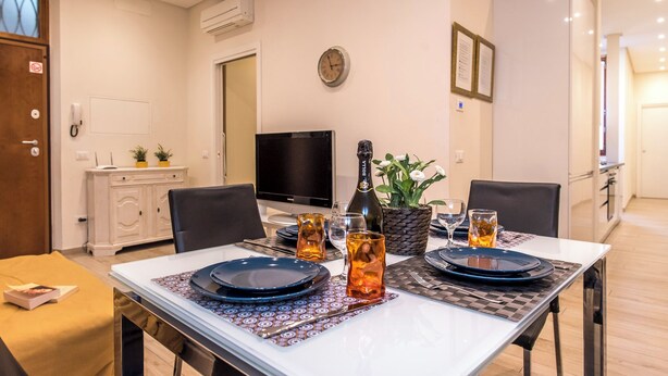 A dining area with a table set for two, a bottle of Bolla champagne, and a television in the background. - Antonino 23 - Two Bedroom Apartment, Sleeps 4 (Firenze)