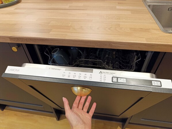 A dishwasher with a control panel and a hand pressing the start button.