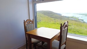 A dining area with a wooden table and chairs, a window with a view of a green landscape and water.