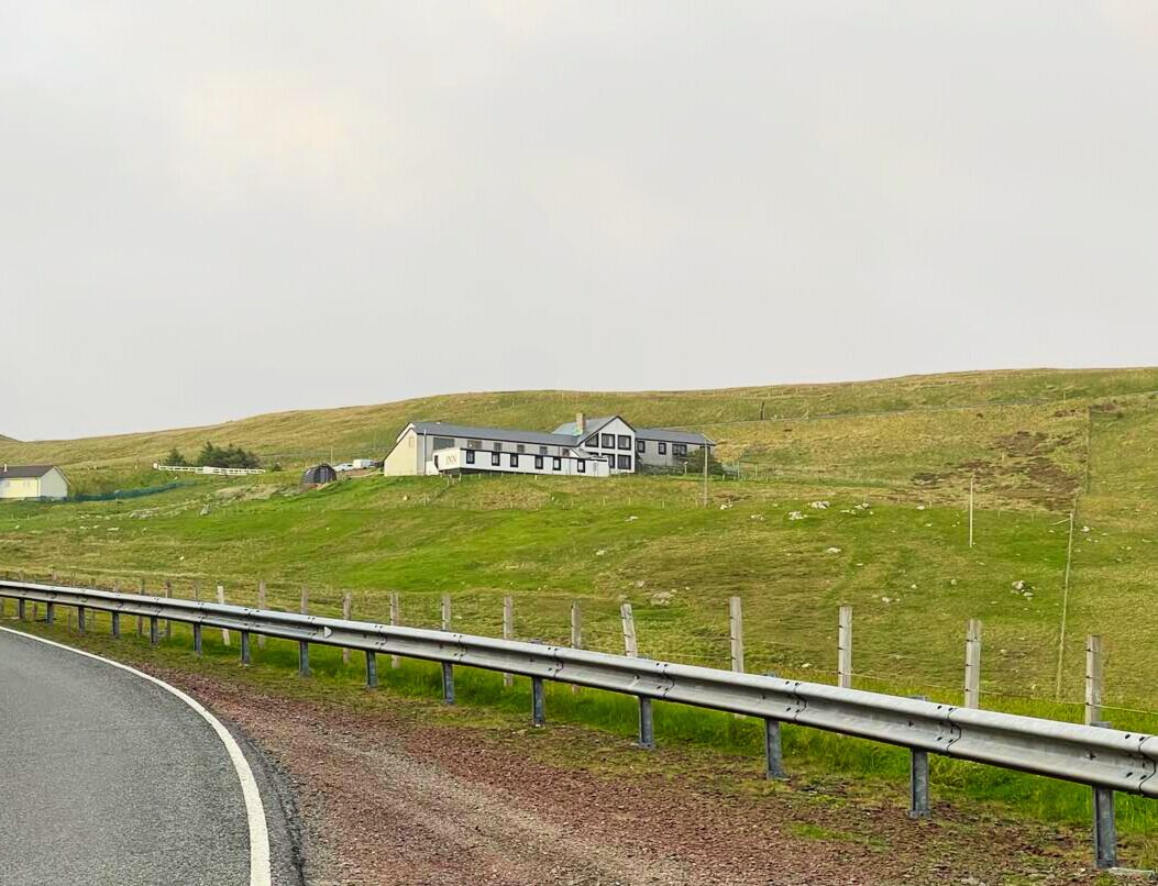 A rural landscape with a large building on a hill, a road with a guardrail, and a fence.