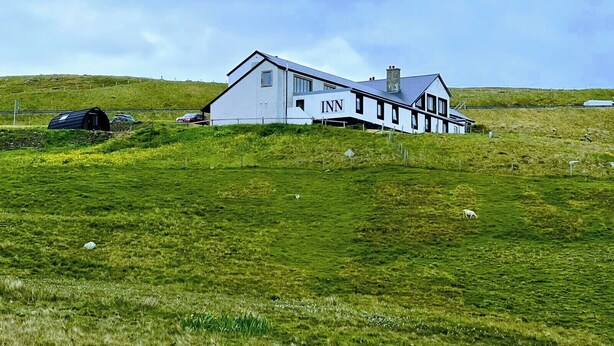 A white building with the sign "INN" on the side, located in a grassy field with a fence in the background.