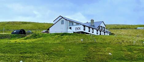 A white building with the sign "INN" on the side, located in a grassy field with a fence in the background.