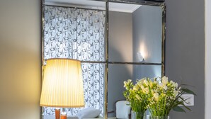 Une console blanche avec un miroir, une lampe et un vase rempli de fleurs.