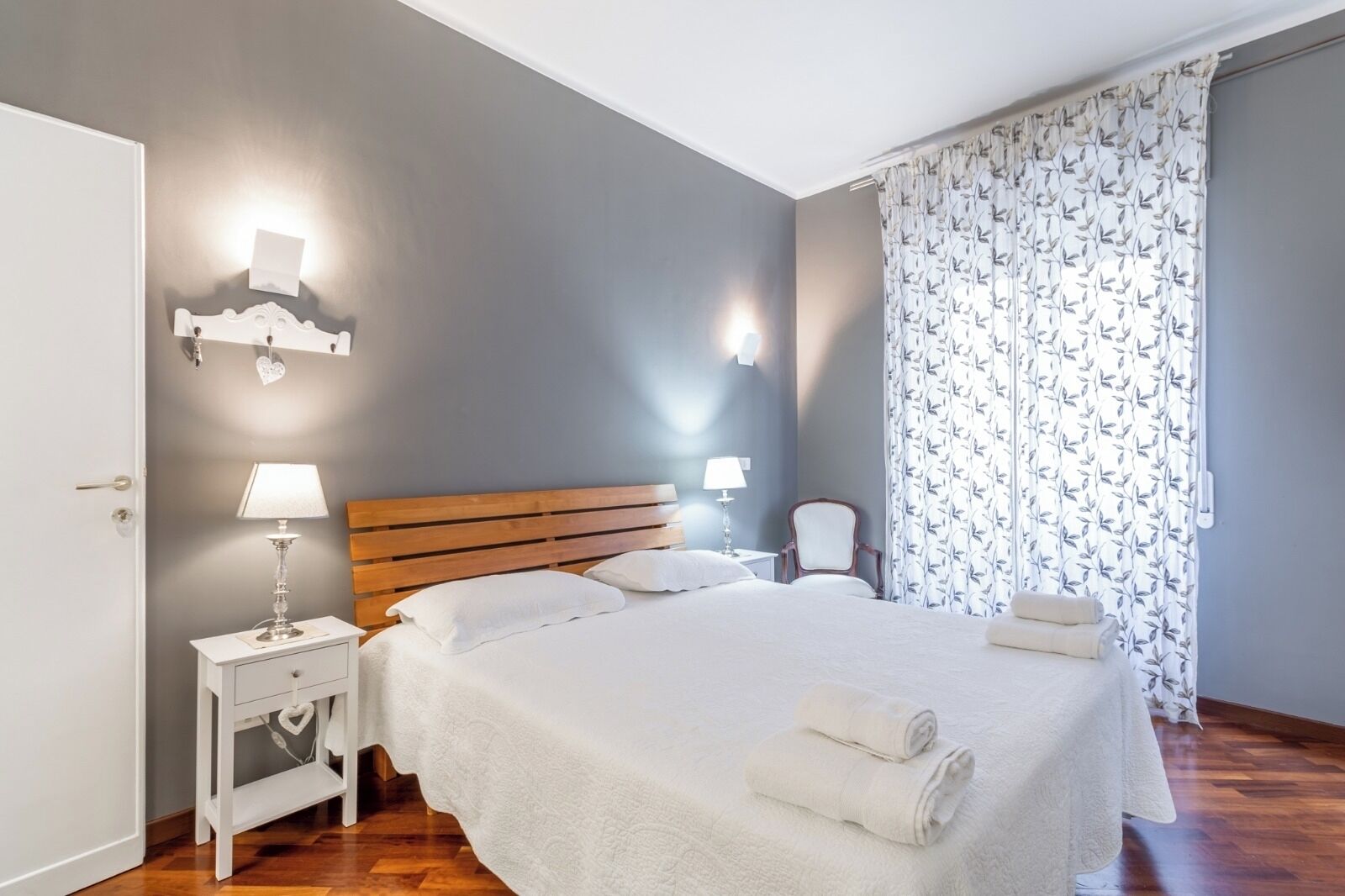 A neatly arranged bedroom with a wooden headboard, a bedside table with a lamp, and a chair.