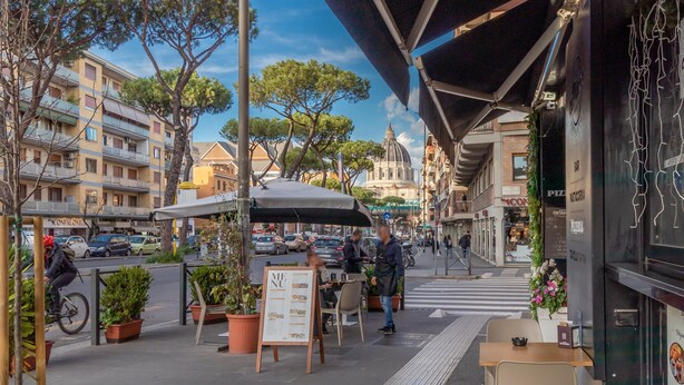 Un café en plein air avec des tables et des chaises, un tableau affichant le menu et des plantes en pot.