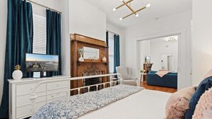 Een slaapkamer met een bed, een dressoir, een televisie, een spiegel en een stoel.