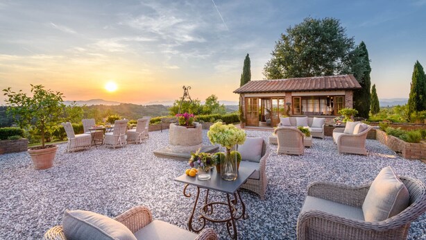 A patio with wicker furniture, a table with flowers, and a view of a house with a tiled roof. - Villa San Miniato Corniano: Iconic 5 Bedrooms Farmhouse with Pool (San Miniato)