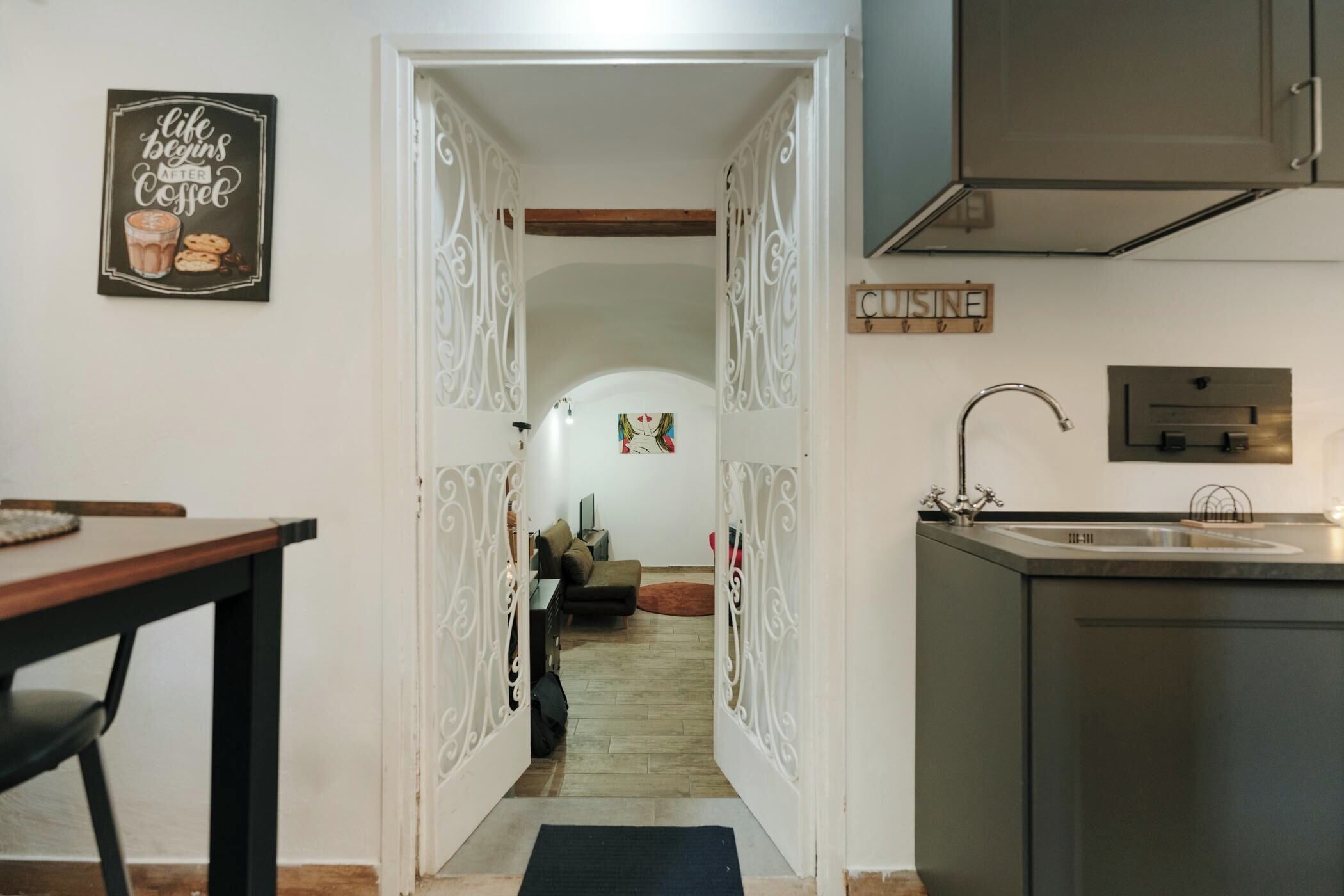 Una cocina con un lavamanos de acero inoxidable, una mesa de comedor con sillas y un cartel decorativo en la pared.