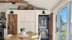 A modern kitchen with a wooden dining table, white cabinets, and a built-in washer and dryer. - ✨ The Dream Cottage– Sea front w/ Hot Tub & Sunset Views - near Parlee Beach (Shediac)