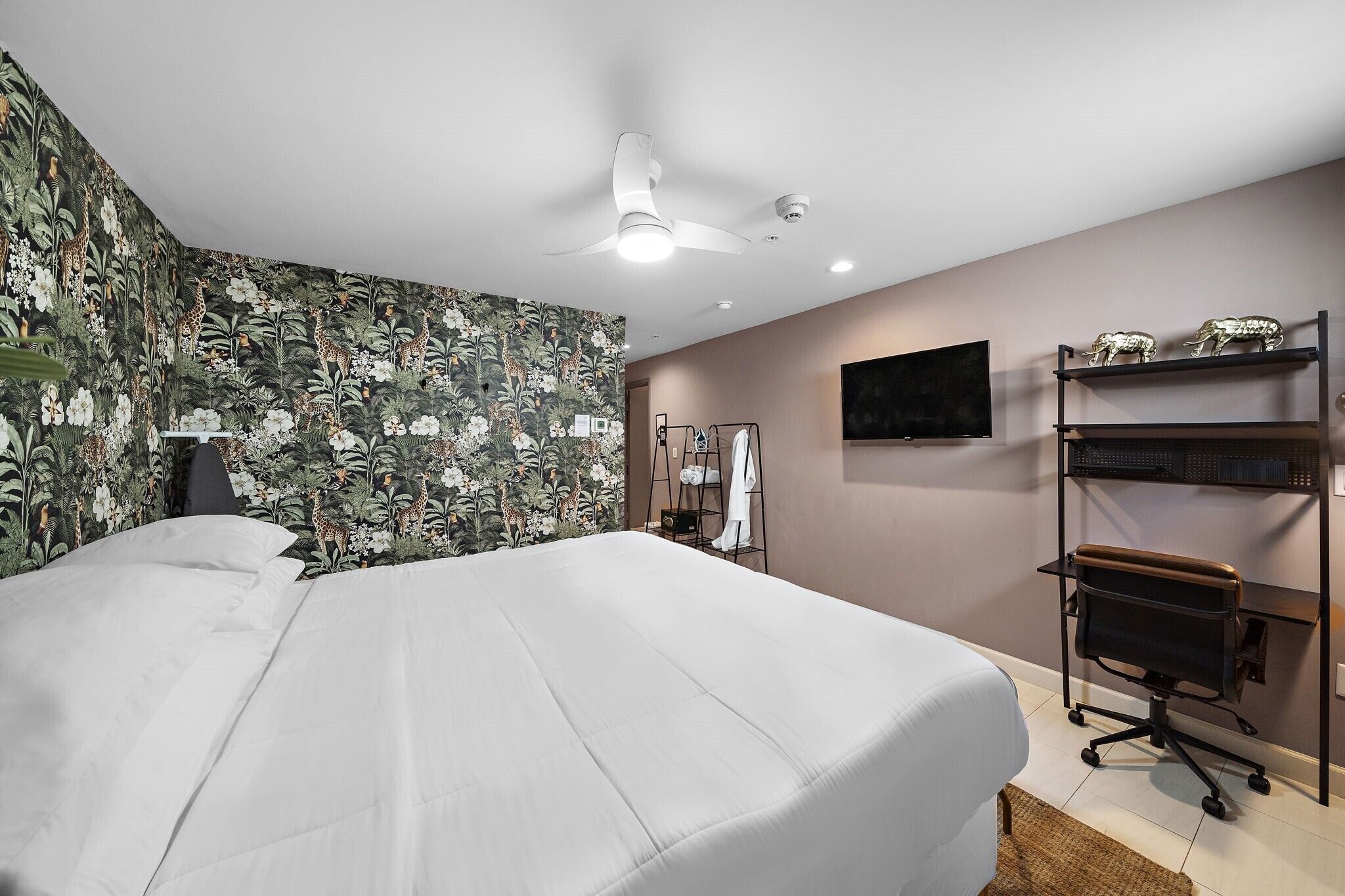 A bedroom with a bed, a ceiling fan, a TV, and a shelf with decorative items.