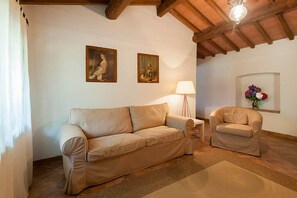 A living room with a sofa, a chair, a lamp, and two paintings on the wall.