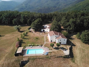 A property with a swimming pool, a white building, and surrounding greenery.