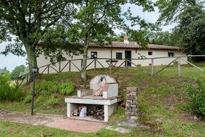 A rustic outdoor grill area with a stone bench, a wooden table, and a metal fence.