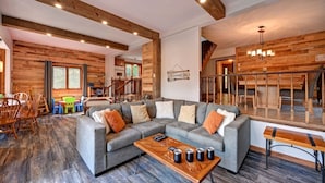 A spacious living area with a large gray sectional sofa, wooden beams on the ceiling, and a wooden coffee table with candles.