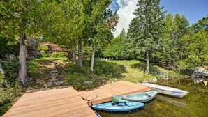 A wooden dock with boats, surrounded by trees and a house in the background.