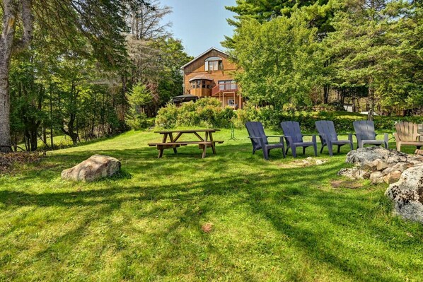 Una casa de madera con balcón, rodeada de abundante vegetación y una mesa de picnic con sillas.