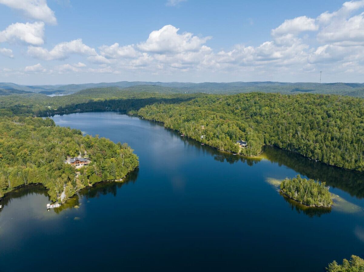 Vista aérea de un lago rodeado de bosques densos, con una casa pequeña en la orilla izquierda.