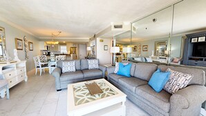 Un salon spacieux avec deux canapés gris, une table basse blanche et un coin repas comprenant une table et des chaises blanches.