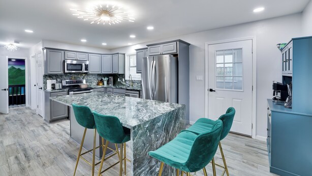 Una cocina moderna con gabinetes grises, un refrigerador de acero inoxidable y una isla de mármol con taburetes de bar.
