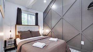 Un dormitorio moderno con una cama grande, mesitas de noche, un ventanal con cortinas y un diseño geométrico en la pared.