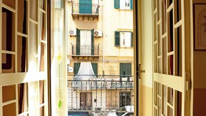 An open door leading to a balcony with a view of a building with multiple windows and shutters. - Butera Apartments Luxury (Palermo)